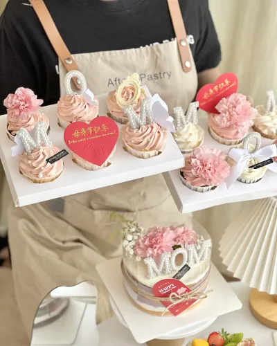 Freshly baked Mother’s Day cupcakes with buttercream and 'MOM' floral toppers in dome packaging